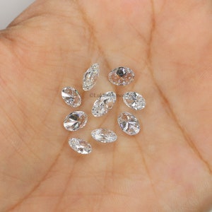 May include: A collection of oval-shaped, clear diamonds, scattered on a hand. The diamonds are various sizes and have a brilliant sparkle.