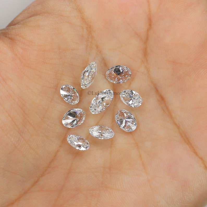 May include: A collection of oval-shaped, clear diamonds, scattered on a hand. The diamonds are various sizes and have a brilliant sparkle.