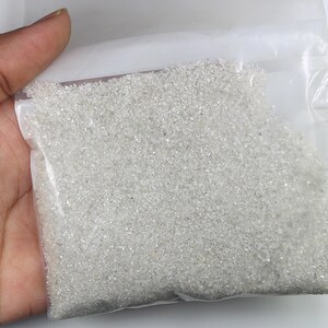 Pu&ograve; includere: Un sacchetto di plastica trasparente riempito con una grande quantit&agrave; di piccoli granuli cristallini bianchi e traslucidi. Il contenuto appare come particelle fini simili a sabbia con una consistenza riflettente e scintillante.