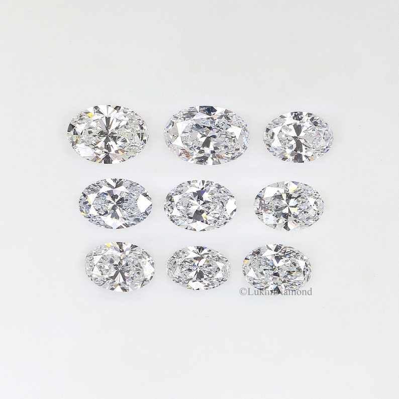 May include: Nine oval-shaped, clear diamonds of varying sizes arranged in three rows on a white background.