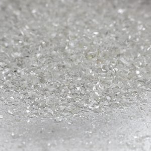 Pu&ograve; includere: Una collezione di piccoli frammenti di vetro trasparente o minerali frantumati, traslucidi e riflettenti. Le particelle sono di forma irregolare, di dimensioni variabili e possiedono un aspetto cristallino brillante che cattura la luce.