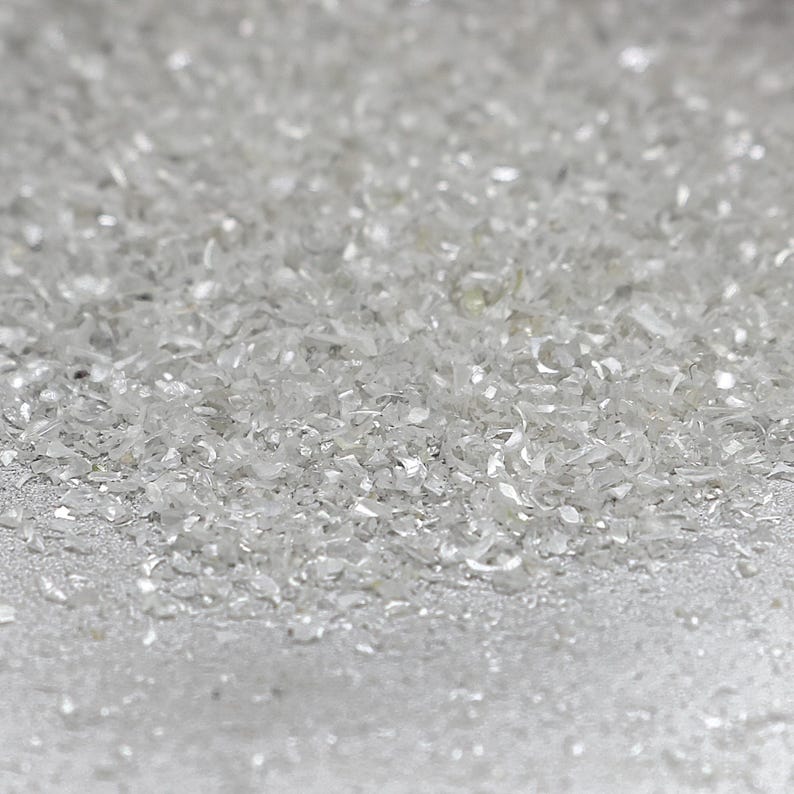 Pu&ograve; includere: Una collezione di piccoli frammenti di vetro trasparente o minerali frantumati, traslucidi e riflettenti. Le particelle sono di forma irregolare, di dimensioni variabili e possiedono un aspetto cristallino brillante che cattura la luce.