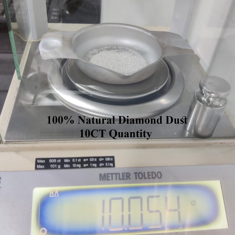 Pu&ograve; includere: Una vaschetta di pesata in metallo argentato contenente polvere di diamante fine, bianca e granulare, posizionata su una bilancia digitale Mettler Toledo. Il display mostra 10,054 ct. Il testo recita 100% Natural Diamond Dust 10CT Quantity.