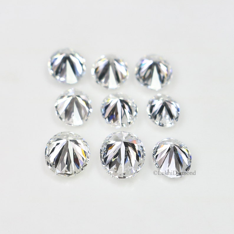 May include: A collection of eight round, clear, faceted gemstones. The gemstones are arranged in two rows on a white surface.