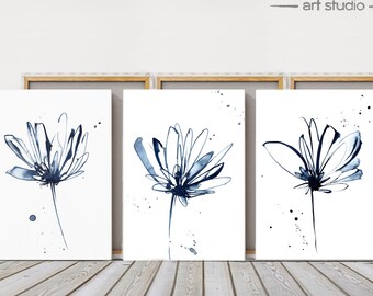 May include: Three framed floral art prints. Each print features a watercolor-style depiction of a flower in shades of blue and black against a white background. The prints are displayed on a wooden floor.
