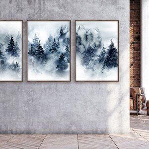 May include: Three framed watercolor prints depict a misty forest scene in shades of blue and gray. The artwork features stylized evergreen trees and a soft, atmospheric effect, suitable for home decor.
