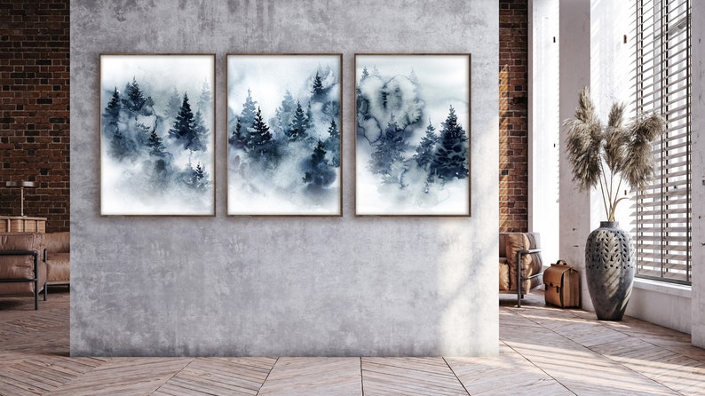 May include: Three framed watercolor prints depict a misty forest scene in shades of blue and gray. The artwork features stylized evergreen trees and a soft, atmospheric effect, suitable for home decor.