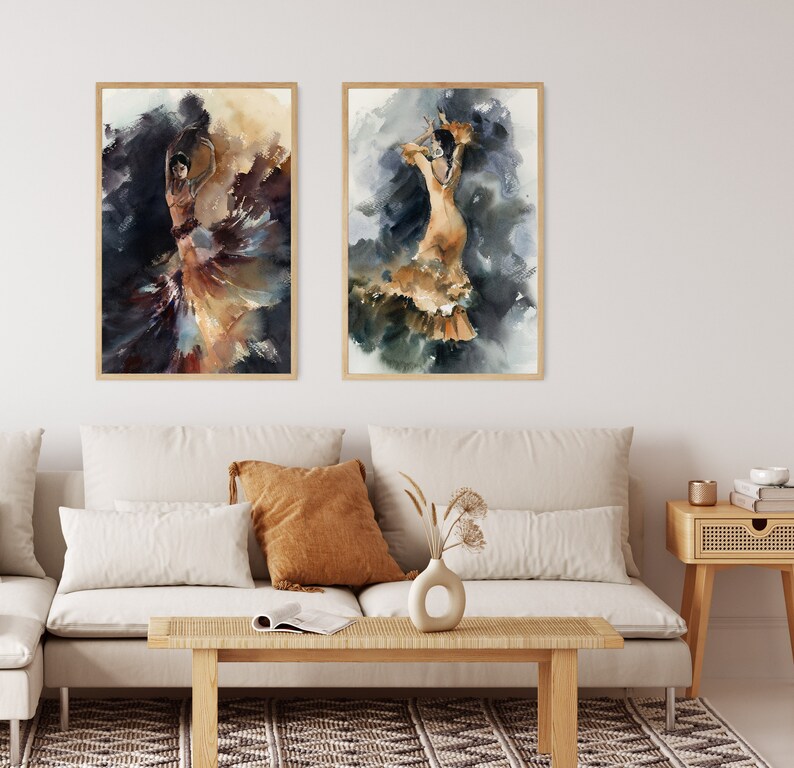 May include: Two framed watercolor paintings of flamenco dancers. The dancers are depicted in flowing dresses with dynamic poses, set against a backdrop of dark and golden hues. The artwork is displayed above a beige sofa with decorative pillows.