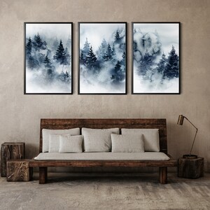 May include: Three framed watercolor prints depicting a misty forest scene in shades of blue and gray. The artwork is displayed above a wooden bench with gray cushions, complemented by a wooden side table and a modern lamp.