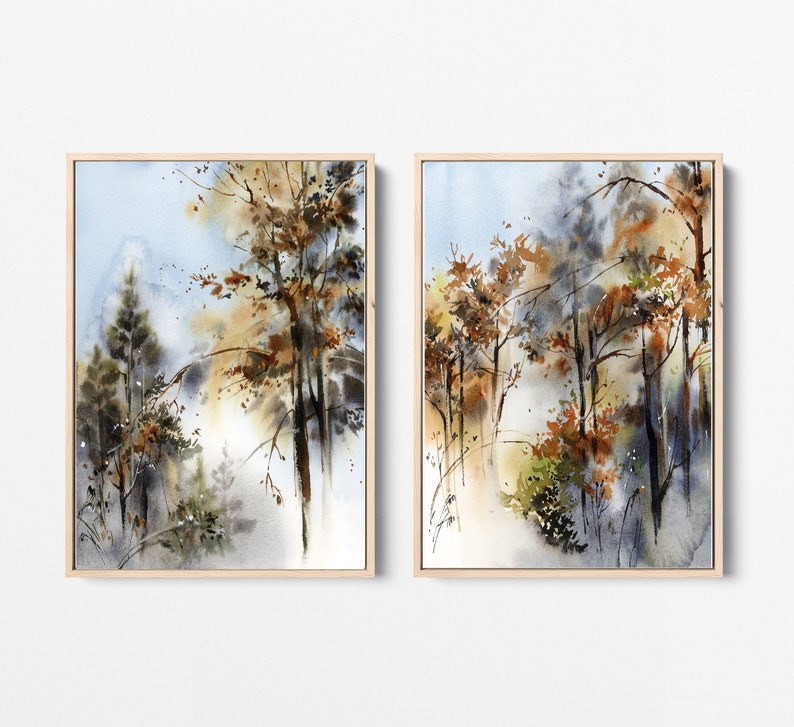Pu&ograve; includere: Due dipinti ad acquerello incorniciati raffiguranti una scena di foresta. L'opera presenta alberi con foglie marroni e arancioni, su uno sfondo blu e bianco tenue. I dipinti sono in cornici di legno color chiaro.