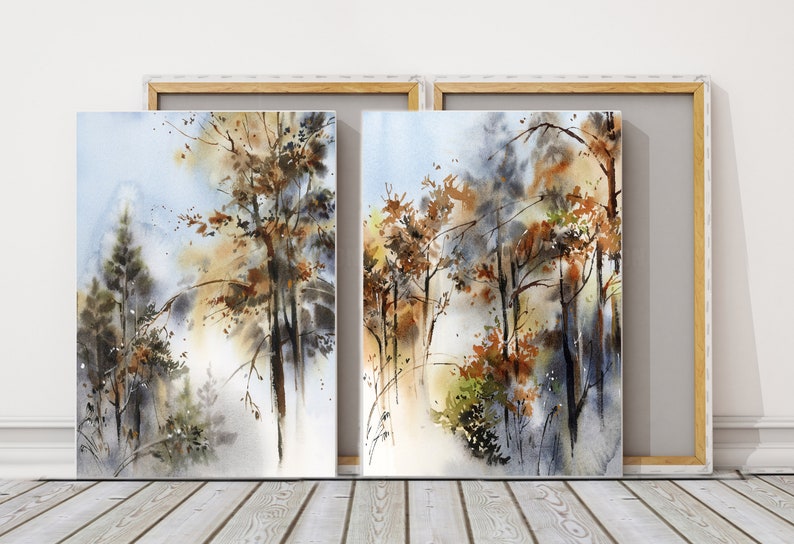 Pu&ograve; includere: Due dipinti ad acquerello incorniciati di una scena di foresta. L'opera presenta alberi con foglie marroni e arancioni, su uno sfondo azzurro chiaro e bianco. I dipinti sono esposti su un pavimento in legno.