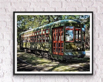 May include: A vintage green and red streetcar with the number 940 on the side, traveling through a tree-lined street. The streetcar has large windows and a sign that reads "New Orleans Streetcar".