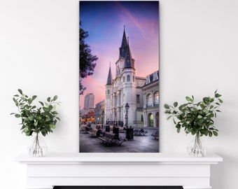 May include: A white building with a tall spire against a pink and purple sunset sky. The building is surrounded by trees and people walking on the sidewalk.