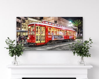 May include: A red vintage streetcar with yellow trim and windows, traveling down a street at night. The streetcar is decorated with a sign that reads "French Quarter Festival 2018".