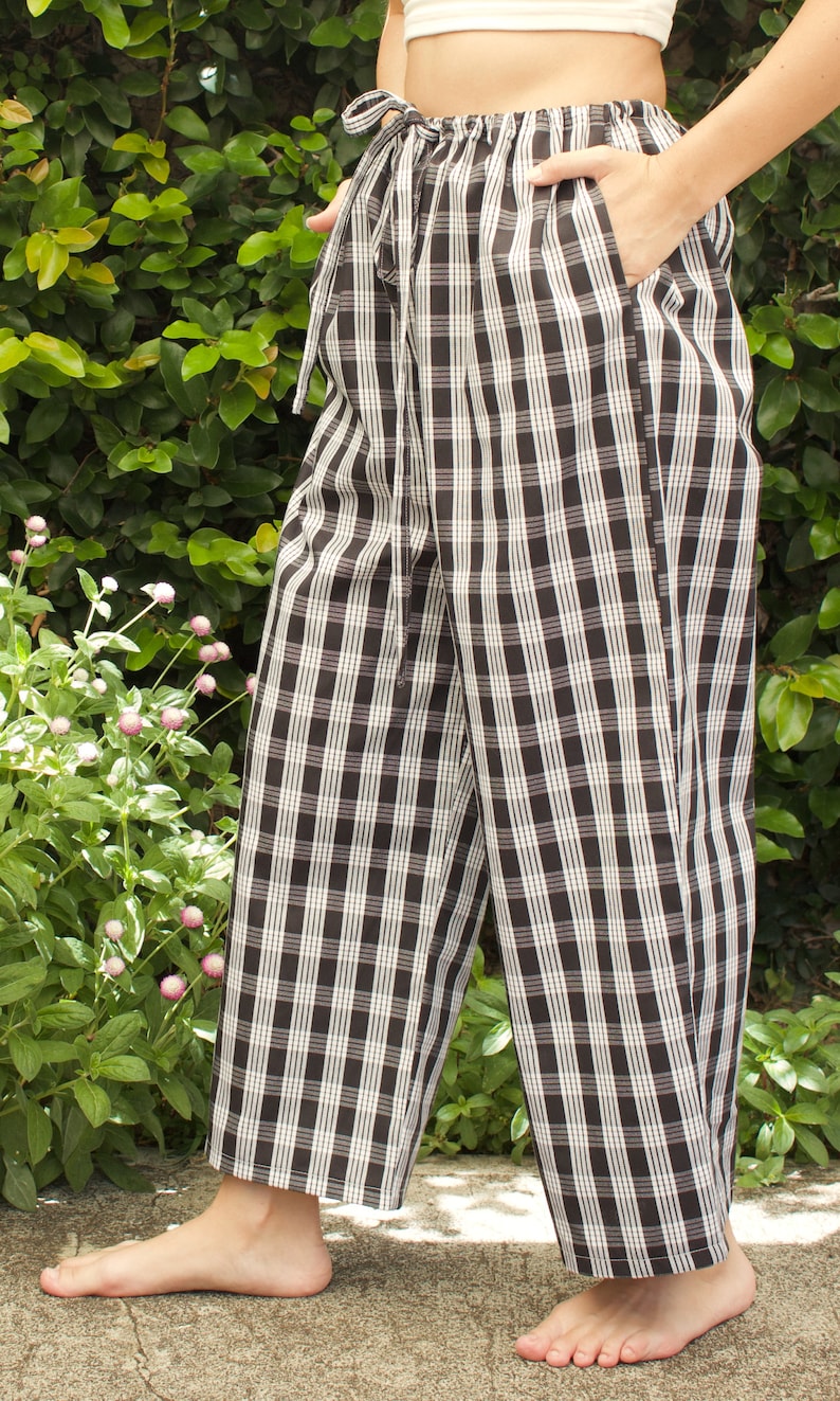 Pu&ograve; includere: Pantaloni a quadri neri e bianchi con vita a coulisse. I pantaloni sono a gamba larga e hanno una vestibilit&agrave; rilassata.