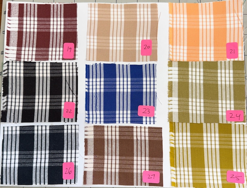 May include: A grid of nine fabric swatches featuring various plaid patterns in colors including maroon, tan, orange, black, blue, olive green, navy, and brown. Each square swatch is labeled with a pink tag numbered from 19 through 27.