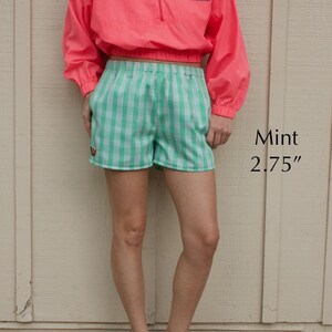 May include: A neon pink long-sleeve pullover with a quarter-zip closure and a blue stingray graphic, paired with mint green and white checkered shorts featuring a small emblem. The text Mint 2.75" is visible on the right side of the image.