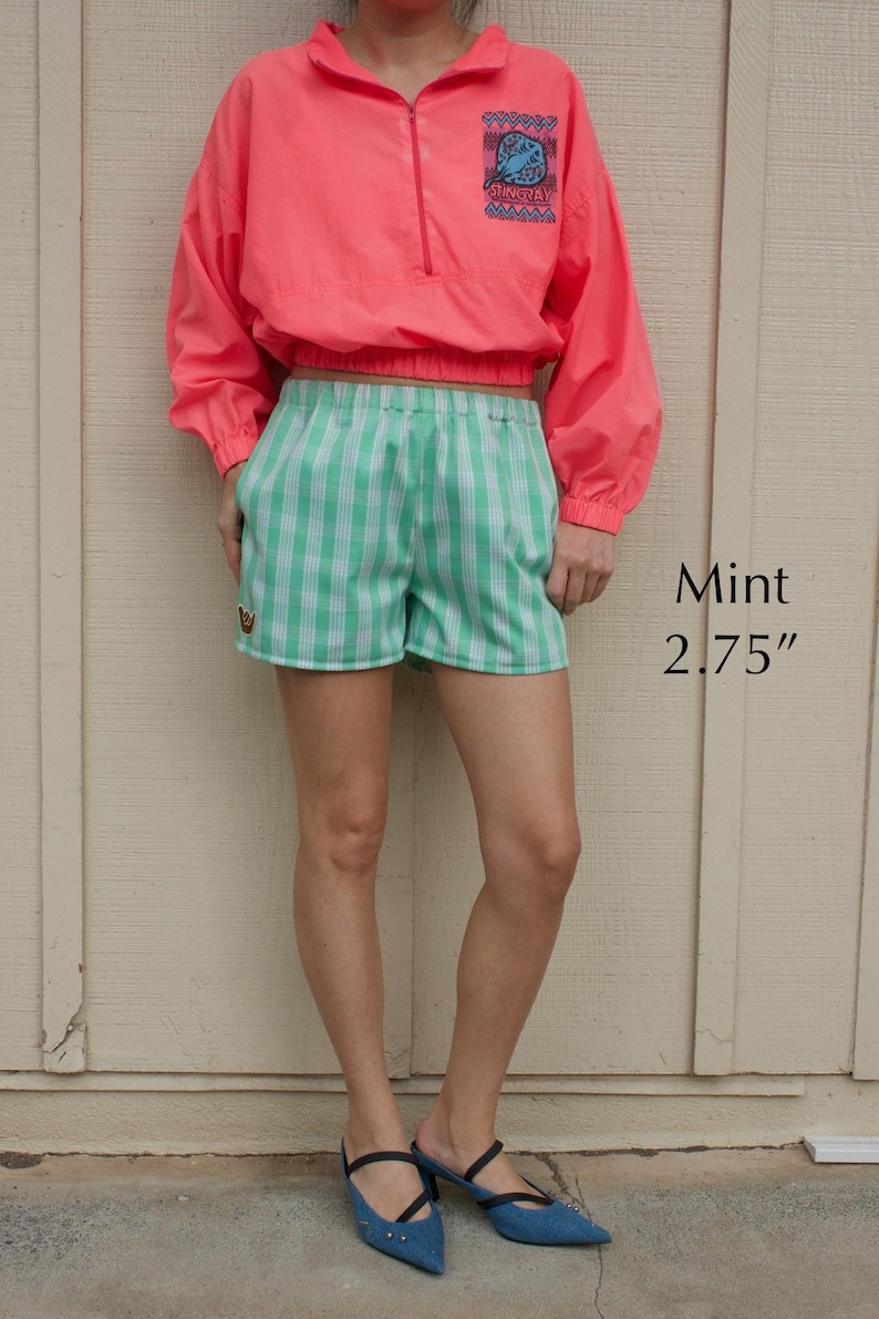 May include: A neon pink long-sleeve pullover with a quarter-zip closure and a blue stingray graphic, paired with mint green and white checkered shorts featuring a small emblem. The text Mint 2.75" is visible on the right side of the image.