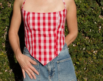 May include: A red and white plaid halter top with a square neckline and a pointed hemline, paired with a blue denim skirt featuring two large front patch pockets. The top has thin straps that tie behind the neck.