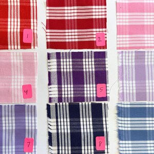 May include: Nine fabric swatches arranged in a grid, each featuring a white plaid pattern. The colors include red, pink, purple, and blue shades. Each swatch is labeled with a pink tag numbered one through nine, indicating distinct color variations.
