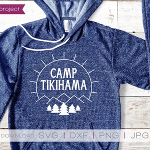 May include: A navy blue hoodie featuring the text "CAMP TIKIHAMA" in white, set within a sunburst design, with mountain and tree graphics. The hoodie has a drawstring and a front pocket.