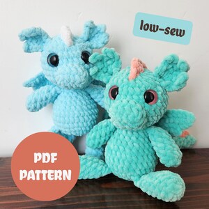 May include: Two plush crochet dragons in shades of blue and teal. The dragons have large black eyes, small wings, and horns. One dragon has a pink accent. The image includes the text "low-sew" and "PDF PATTERN".