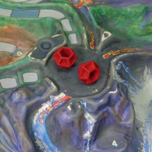 May include: Two red, geometric dice with a hexagonal shape are on a colorful game board.