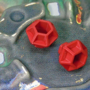 May include: Two red plastic geometric shapes with a hexagonal hole in the center. The shapes are similar in size and design.