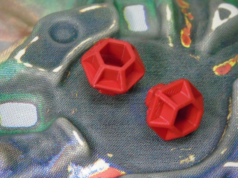 May include: Two red plastic geometric shapes with a hexagonal hole in the center. The shapes are similar in size and design.