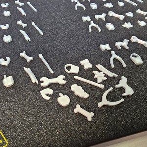 May include: A collection of white plastic 3D printed shapes, including bones, wrenches, and other abstract shapes.