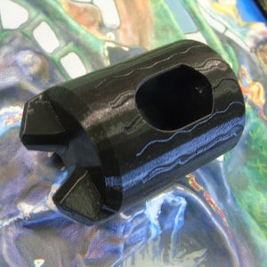 May include: A black plastic 3D printed object with a hexagonal shape and a hole in the center. The object has a textured surface.