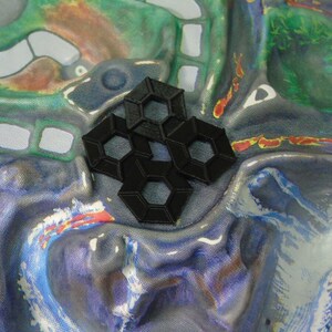 May include: A close-up of a black plastic hexagonal tile set. The tiles are arranged in a pattern and are on a colourful fabric background.