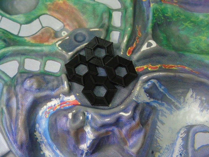 May include: A close-up of a black plastic hexagonal tile set. The tiles are arranged in a pattern and are on a colourful fabric background.