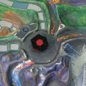 May include: A black hexagonal game piece with a red centre, sitting on a blue and purple game board.