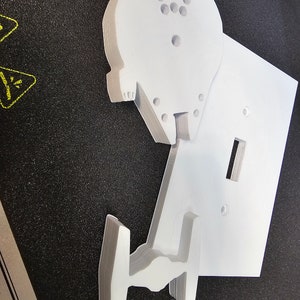 May include: White plastic light switch cover with a 3D printed Millennium Falcon design. The Falcon is layered and has a detailed design.