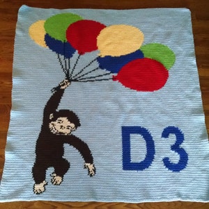 May include: A blue crocheted blanket with a monkey holding balloons and the text "D3" in blue.