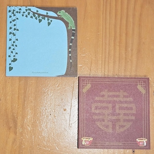 May include: Two blank notepads with different designs. The first notepad has a blue background with a green lizard on a branch with green leaves. The second notepad has a red background with a gold Chinese character. The text on the first notepad reads "Zhudorwoohoo".