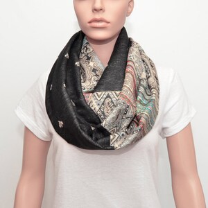 Puede incluir: Una bufanda negra infinita con un estampado paisley colorido. La bufanda está hecha de una tela suave y cómoda y es perfecta para agregar un toque de estilo a cualquier atuendo.