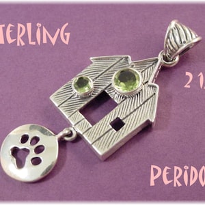 May include: Sterling silver dog house pendant with two green peridot stones. The pendant is 2 1/4 inches tall and features a paw print charm.
