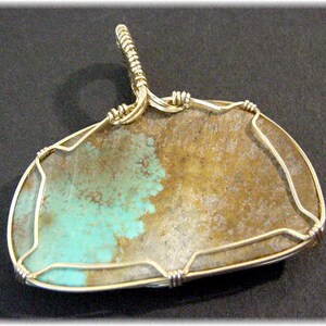 May include: A turquoise and brown stone pendant with a silver wire wrap. The stone is set in a silver wire frame and has a silver bail for hanging.