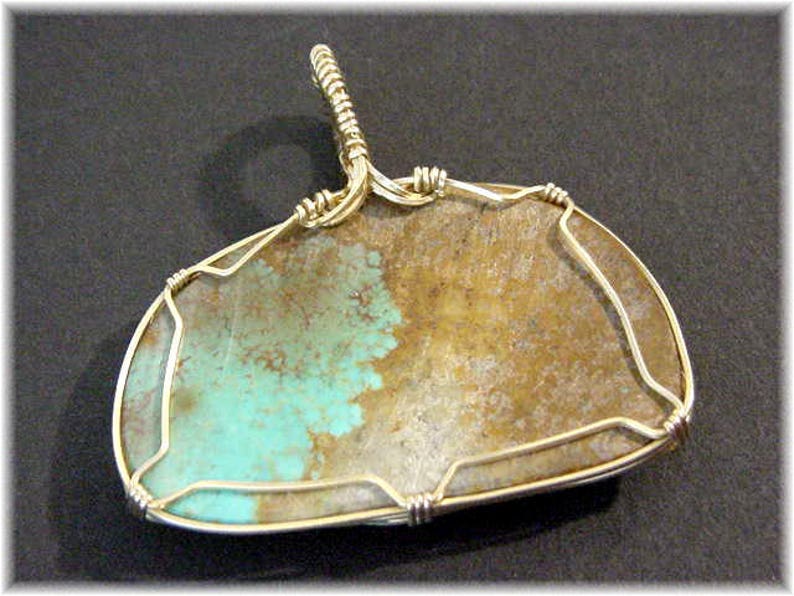May include: A turquoise and brown stone pendant with a silver wire wrap. The stone is set in a silver wire frame and has a silver bail for hanging.