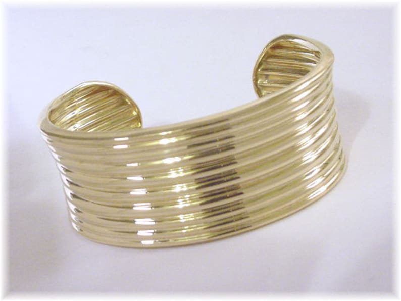May include: A gold-toned bangle bracelet with a ridged design. The bracelet is made of multiple layers of metal that are stacked on top of each other.