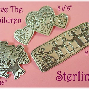 May include: A collection of sterling silver pins with various designs. One pin features a Christmas tree with people, another has people in a heart shape, and a third is a rectangular pin with people holding hands. The text "Save The Children" and "Sterling" are also visible.