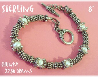 May include: A chunky silver bracelet with a toggle clasp and six white pearls. The bracelet is 8 inches long and weighs 22.86 grams. STERLING is written at the top of the image. CHUNKY 22.86 GRAMS is written at the bottom of the image.