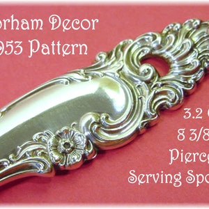 May include: A silver-colored metal serving spoon with an ornate handle featuring a floral motif and a pierced design. The text reads: Gorham Decor 1953 Pattern, 3.2 Ozs, 8 3/8" Pierced Serving Spoon. The spoon has a polished, reflective finish.