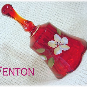 May include: A red glass bell with a white flower design. The bell is made by Fenton.
