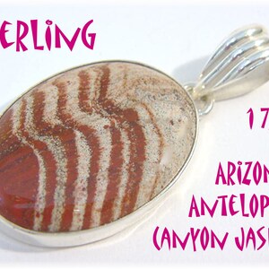 May include: Sterling silver pendant with an oval Arizona Antelope Canyon Jasper stone. The stone features a pattern of red and white stripes. The pendant measures 1 7/8 inches in length.