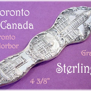 May include: A sterling silver spoon with detailed engravings of Toronto landmarks, including City Hall and the Parliament Buildings. The spoon is 4 3/8 inches long and weighs 12 grams. Text on the spoon reads "Toronto Canada" and "Toronto Horbor".
