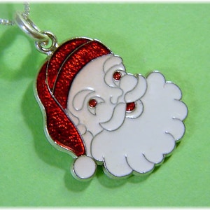 May include: Silver pendant necklace featuring a red and white enamel Santa Claus design. The Santa Claus has a white beard and a red hat.