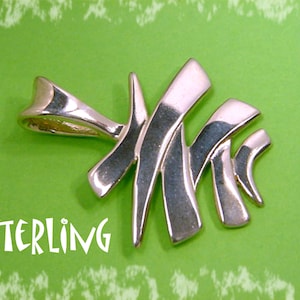 May include: A silver-colored pendant in the shape of a stylized fish skeleton. The pendant has a curved, abstract design with the word "STERLING" in white text. The pendant is set against a bright green background.
